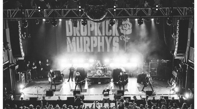 Dropkick Murphys performing live in front of a packed crowd, band banner behind them