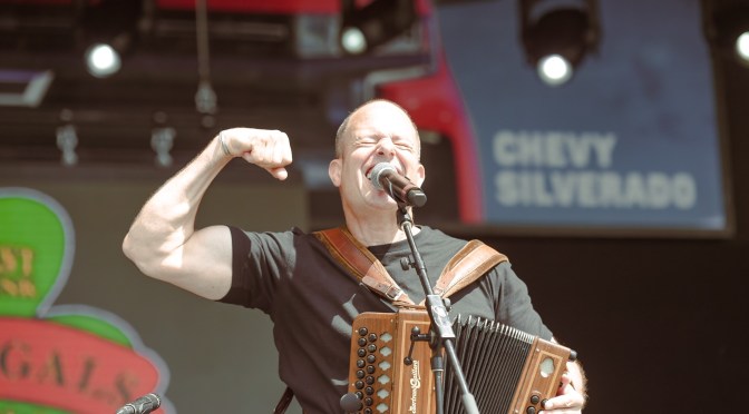 Gregory Grene of The Prodigals singing and playing button accordion on stage, fist raised